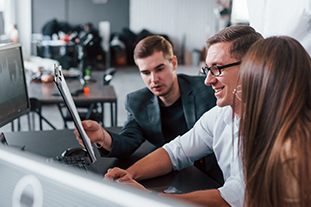 Holds Document In Hands. Team Of Stockbrokers Works In Modern Office With Many Display Screens