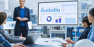 Modern Industrial Factory Meeting: Confident Female Engineer Uses Interactive Whiteboard, Makes Report To A Group Of Engineers, Managers Talks And Shows Statistics, Growth And Analysis Information